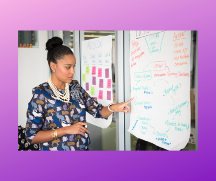 Standing African American woman pointing at a written flow chart of information.